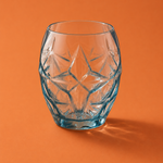 Clear glass tumbler with textured design on an orange background