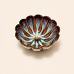 Decorative ceramic bowl with scalloped edge and blue and brown design on a beige background