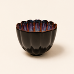 Black ceramic bowl with scalloped edge on a beige background