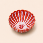 Red ceramic bowl with scalloped edge on a beige background