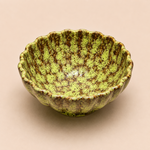 Green ceramic bowl with brown speckles on a beige background