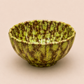 Green ceramic bowl with brown speckles on a beige background