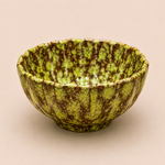 Green ceramic bowl with brown speckles on a beige background