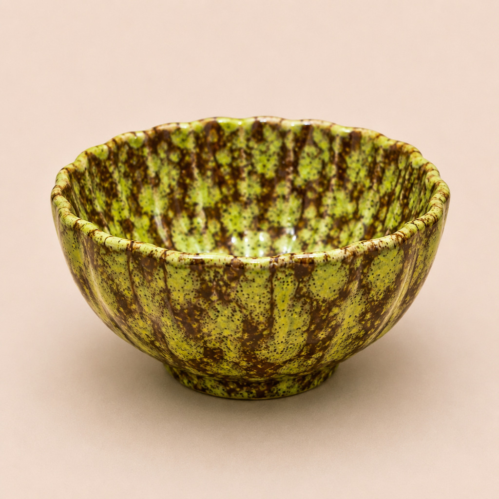 Green ceramic bowl with brown speckles on a beige background