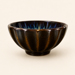 Black ceramic bowl with ribbed texture on a beige background