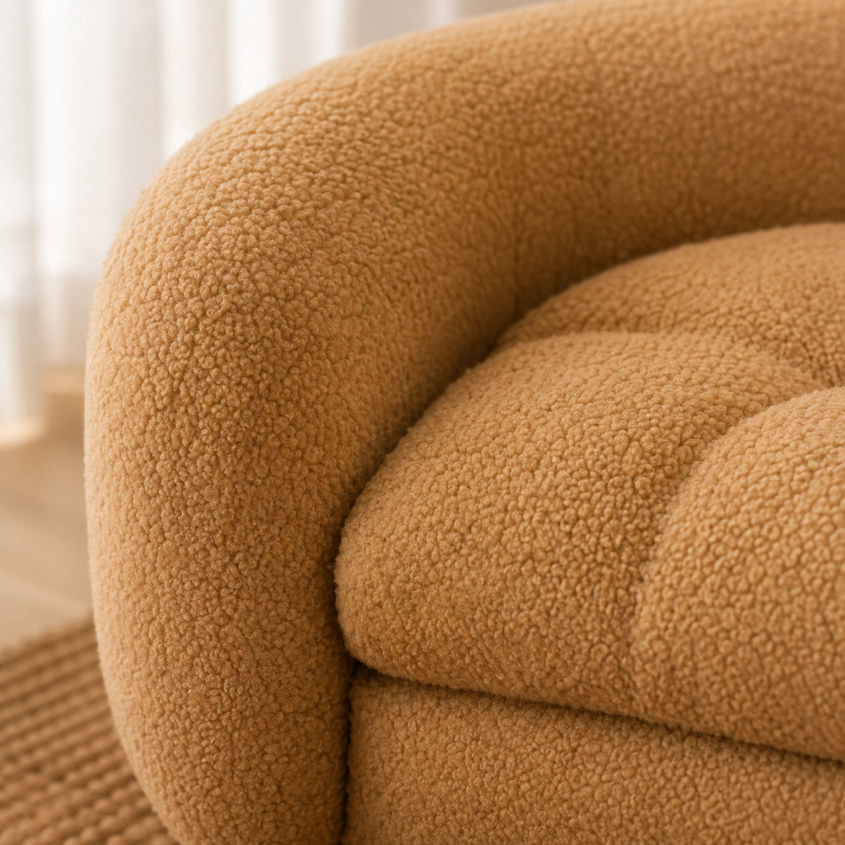 Close-up of a rounded upholstered arm and seat cushion in a warm camel bouclé fabric, with soft natural light and a blurred indoor background. 