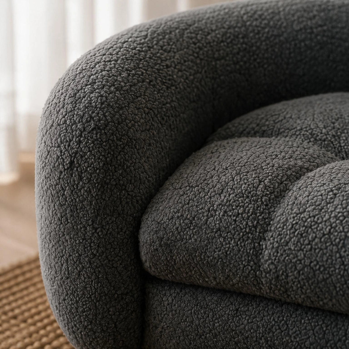Close-up of a dark gray bouclé upholstered armchair, showing the textured fabric and tufted seat cushion in a softly lit interior setting. 