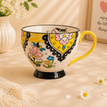 Colorful mug with floral design on a soft surface with flowers and text in the background