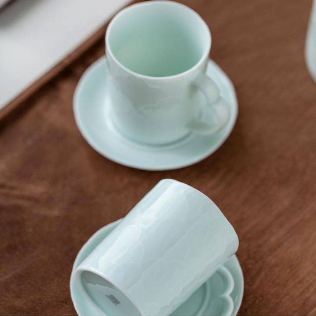 Two light green ceramic cups and saucers on a wooden surface.