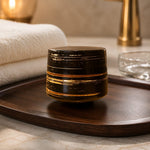 Decorative black and gold cylindrical object on a wooden tray with a blurred background
