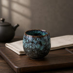 Ceramic cup with blue glaze on a wooden tray with a teapot in the background