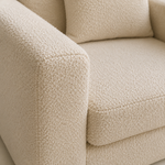 Close-up of a cream-colored bouclé upholstered sofa showing the textured fabric, armrest, seat cushion, and back cushion.