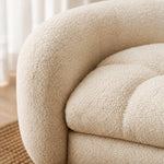 Close-up of a cream-colored bouclé upholstered sofa corner, showing the soft textured fabric and tufted seat cushion in a bright indoor setting. 