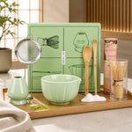 Tea-making set with green bowl, whisk, and other tools on a wooden tray.