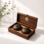 Two brown ceramic pots in a wooden box with a plant in the background
