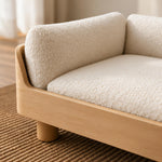 Close-up of a modern low-profile sofa with textured cream bouclé cushions and a light natural wood frame, resting on a woven brown rug.