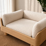 A modern pet sofa bed with a cream-colored textured fleece cushion and a light natural wood frame, styled on a woven rug in a bright room.