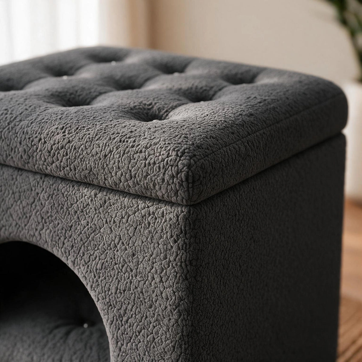 A dark gray tufted storage ottoman with a textured bouclé-like fabric, shown in a close-up view highlighting the button tufting and the side arch opening.